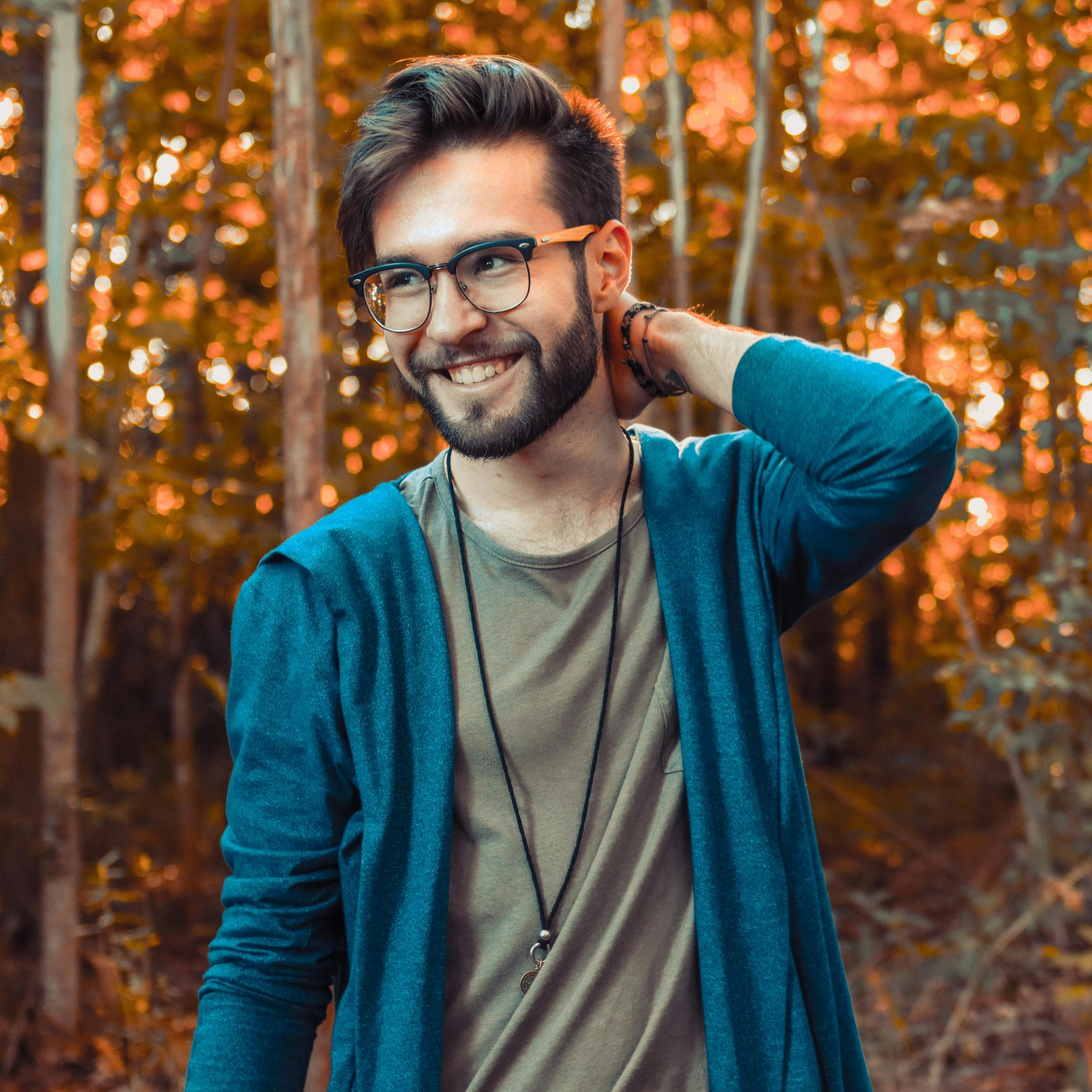 Young man with glasses and beard smiling in a colorful autumn forest.